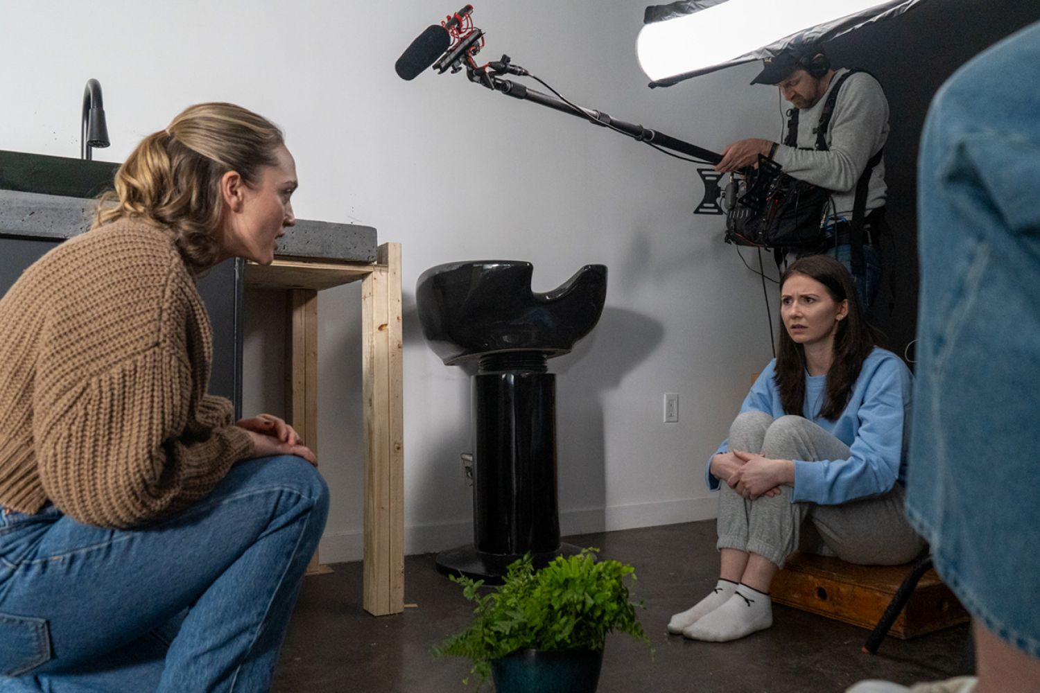 Scene of a two women on the floor, a plant is between them